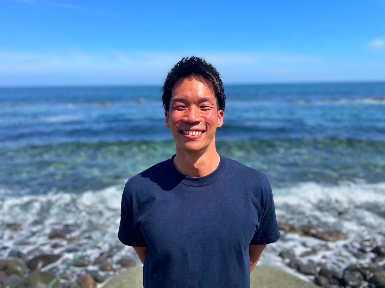 海を背景に笑顔で立つ、ぞのです。